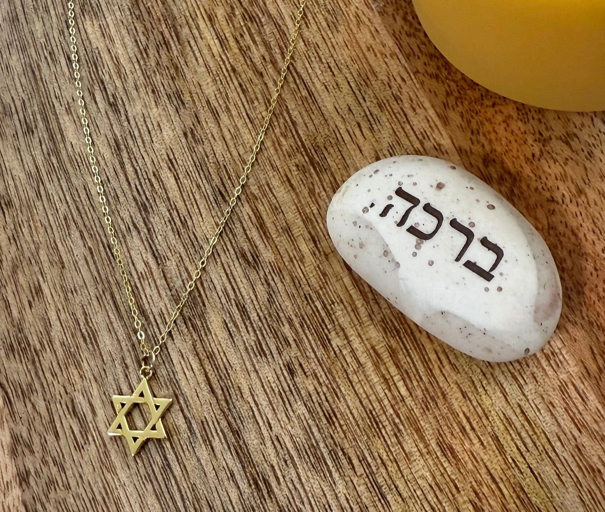 שרשרת מגן דוד בציפוי זהב 14 קראט עם תליון קטן, מונחת לצד אבן ברכה